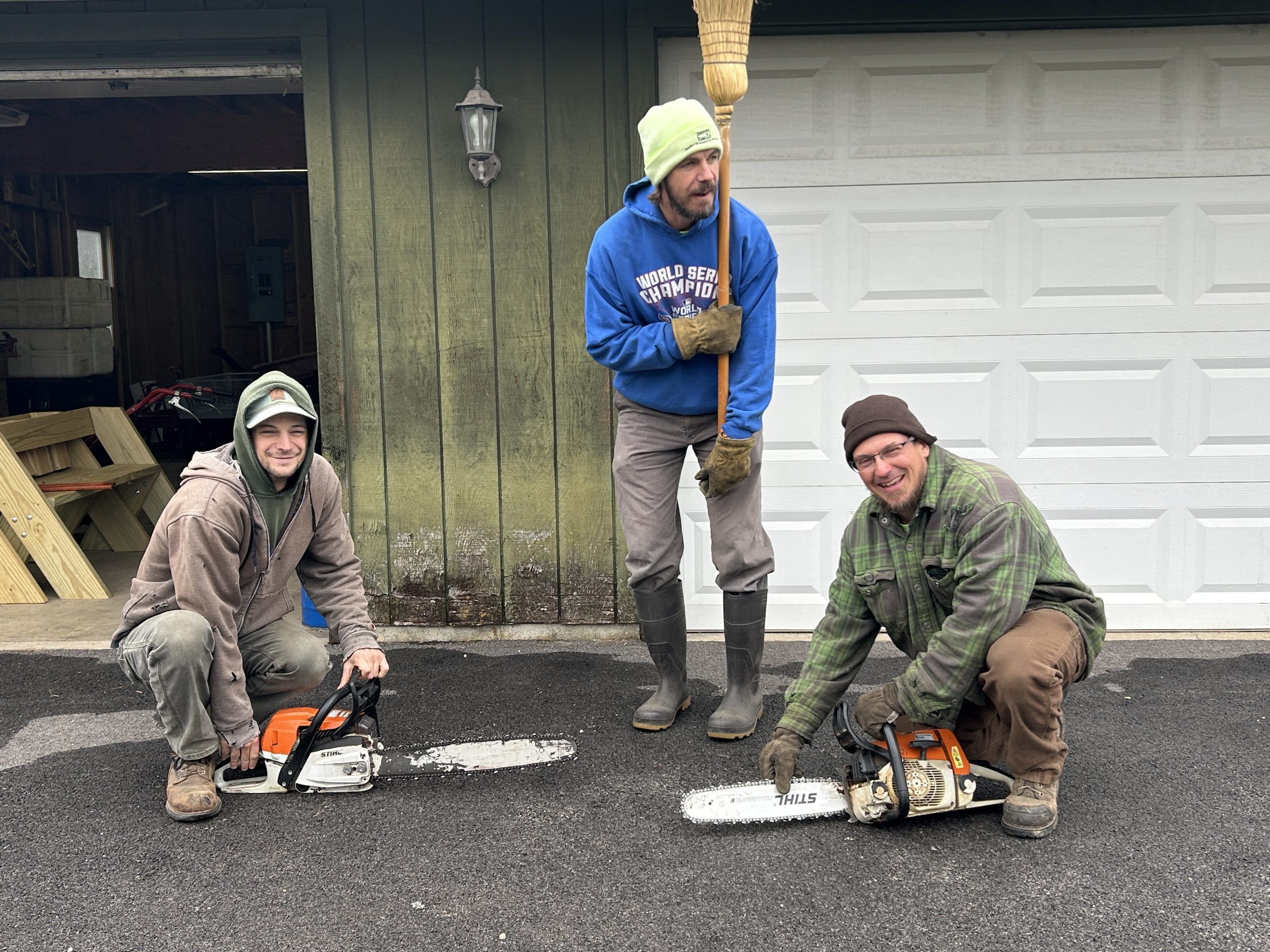Three men outside of a barn with chainsaws.