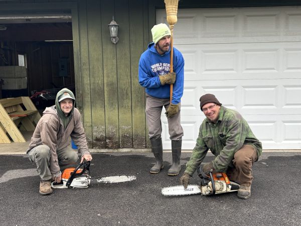 Three men outside of a barn with chainsaws.