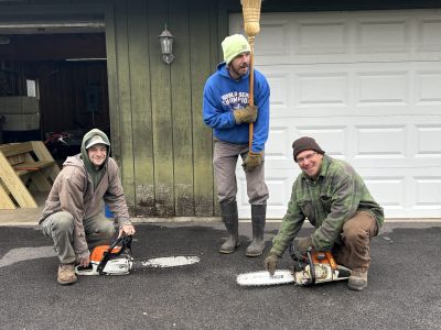 Three men outside of a barn with chainsaws.
