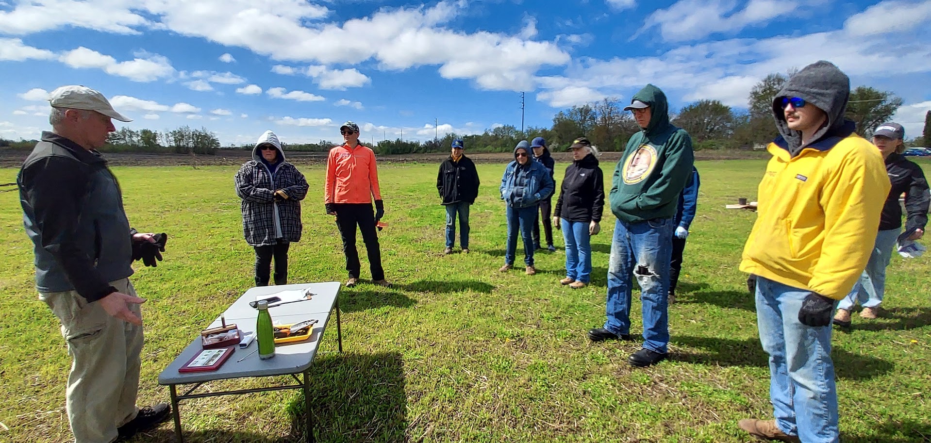 A group of people listening to a speaker outside.