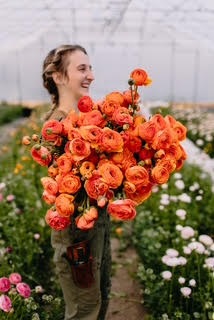 A woman cut flower grower holding a large bouquet of orange flowers. 