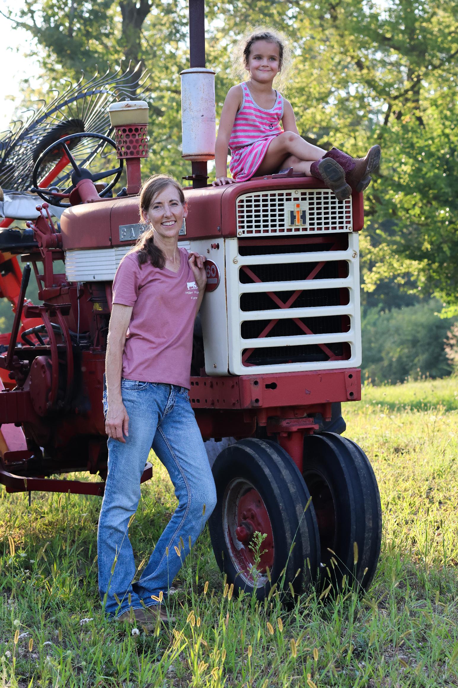A woman farmer and her child posing by a red tractor.
