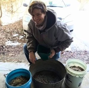 TLC member Jacob Karkowski kneeling by buckets of native seed. 