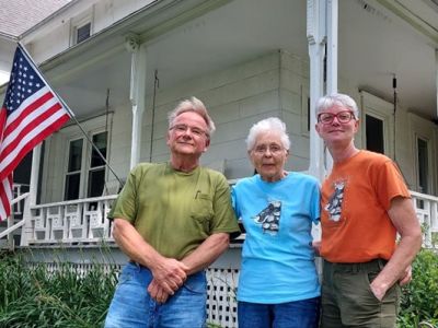 Three people standing in front of a farmhouse
